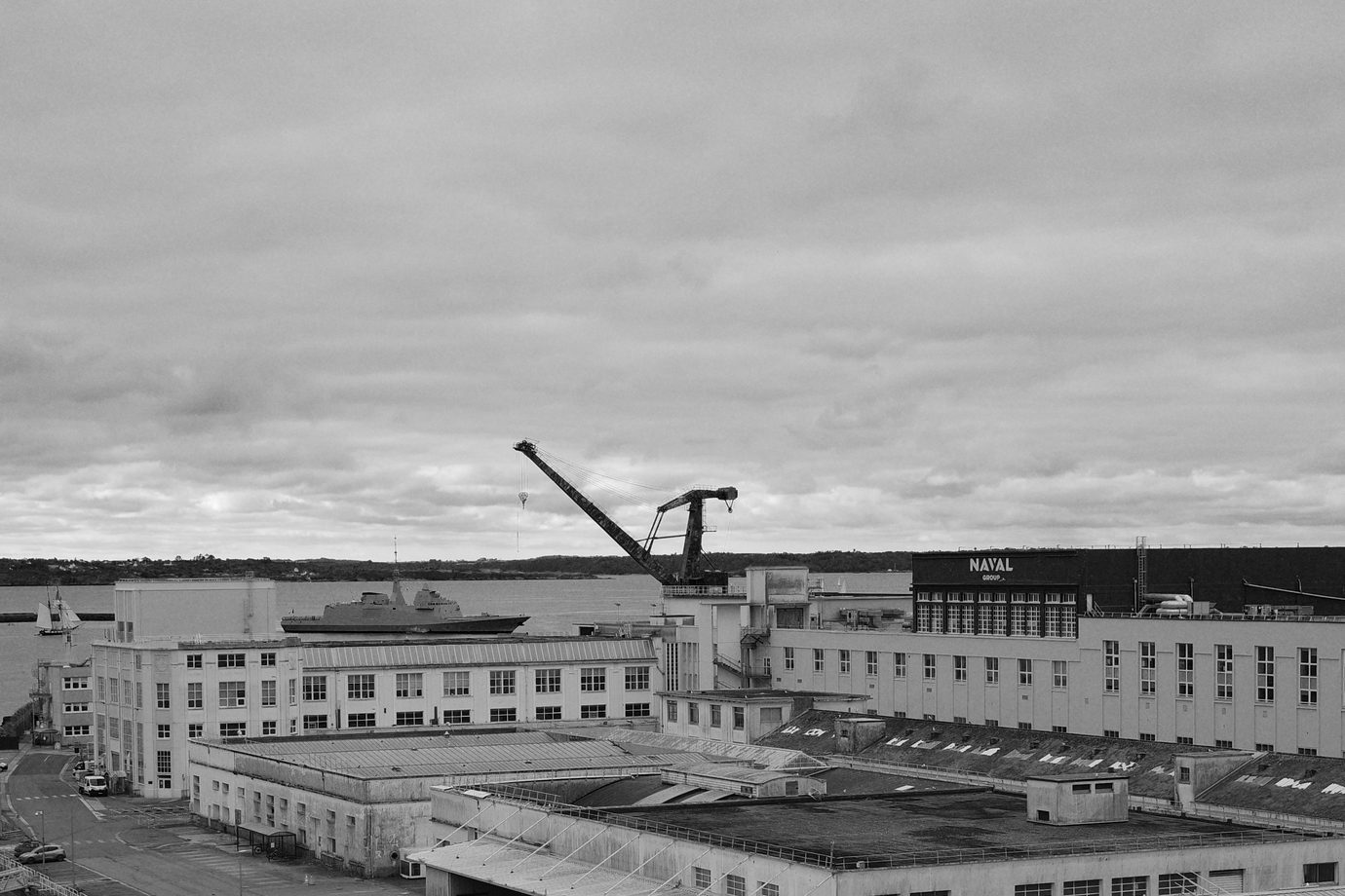 une FREMM rentre à l'arsenal en passant dans les bâtiments Naval Group (même en week-end, le gars reste corporate)